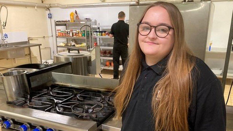 Apprentice chef Ellie (16) standing next to a cooker in her work place