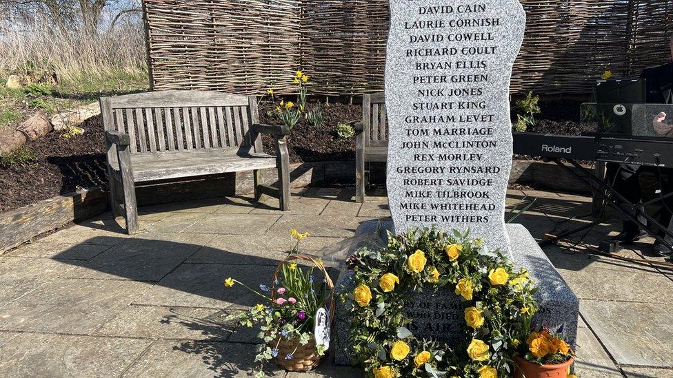 A memorial stone with the names of the crash victims. Flowers are laid at the bottom.