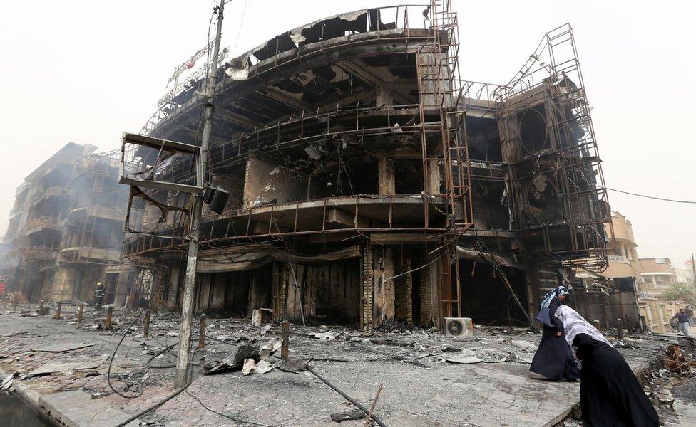 Iraqi women walk past a damaged building at the site of a suicide car bombing claimed by the Islamic State group on July 3, 2016 in Baghdad's central Karrada district