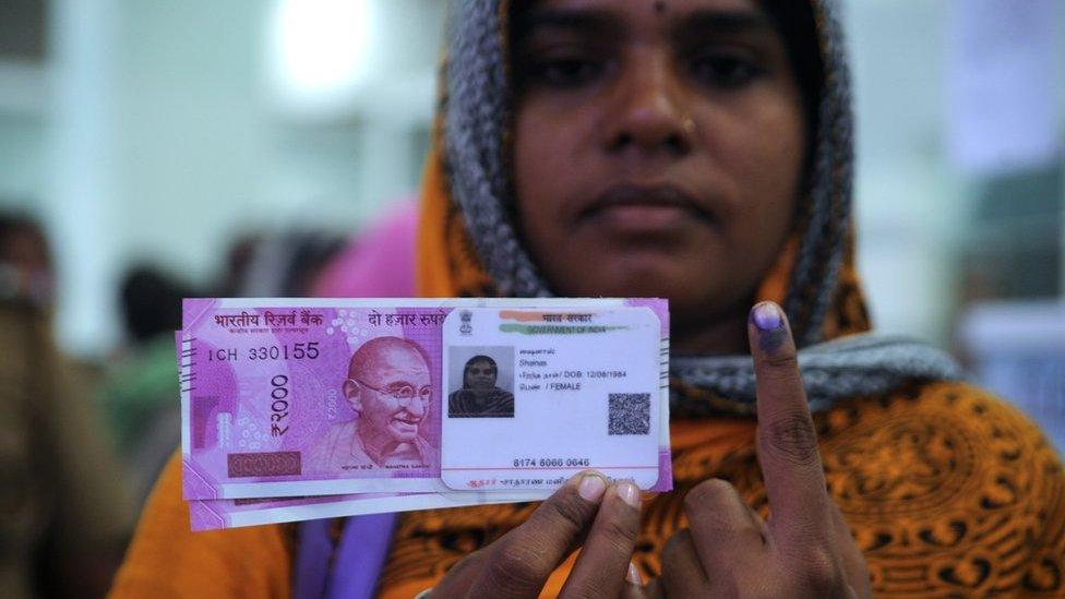 An Indian woman poses with new 2000 rupee notes, her Aadhaar ID card and a finger inked with indelible ink after exchanging withdrawn 500 and 1000 rupee banknotes at a bank in Chennai on November 17, 2016