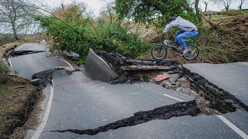 BMX rider jumping off a ledge on a road badly damaged by subsidence