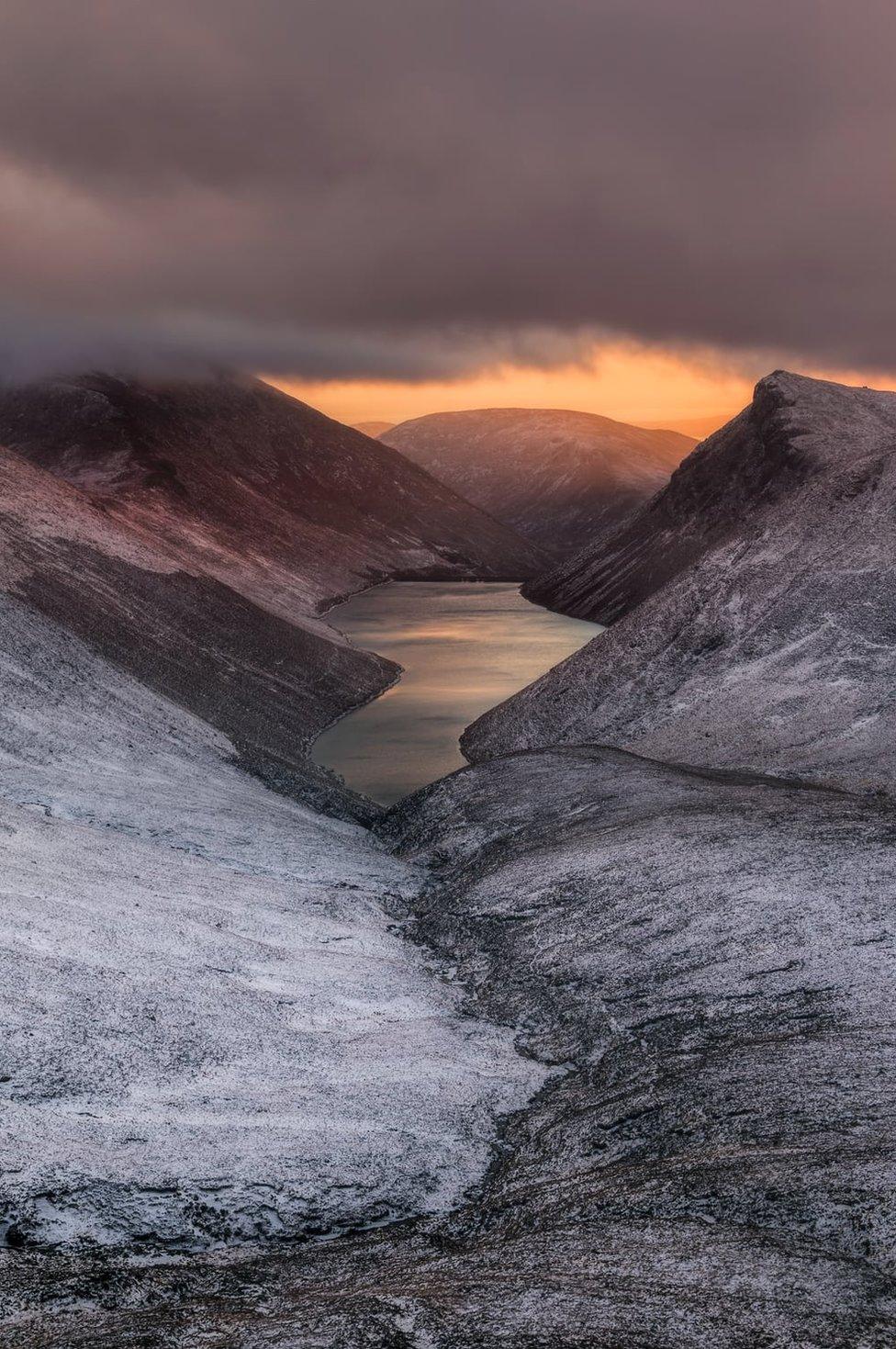 Sunset over Ben Crom reservoir with snow dusting the neighbouring land as seen from Slieve Corragh in the Mourne mountains in County Down