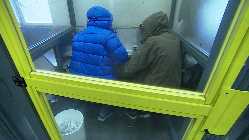 Two people in a glass cubicle