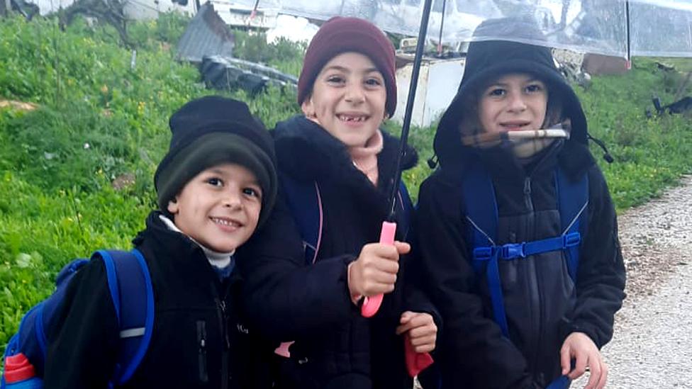 Najjar siblings stand smiling under an umbrella, Amr is at right