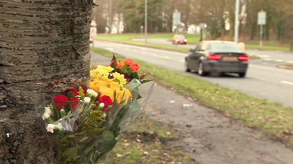 Three bouquets of yellow, red and white flowers tied to a tree beside a road