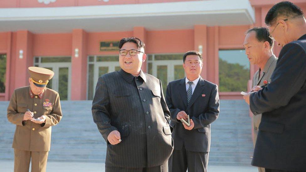 Kim Jong-un smoking a cigarette while officials take notes