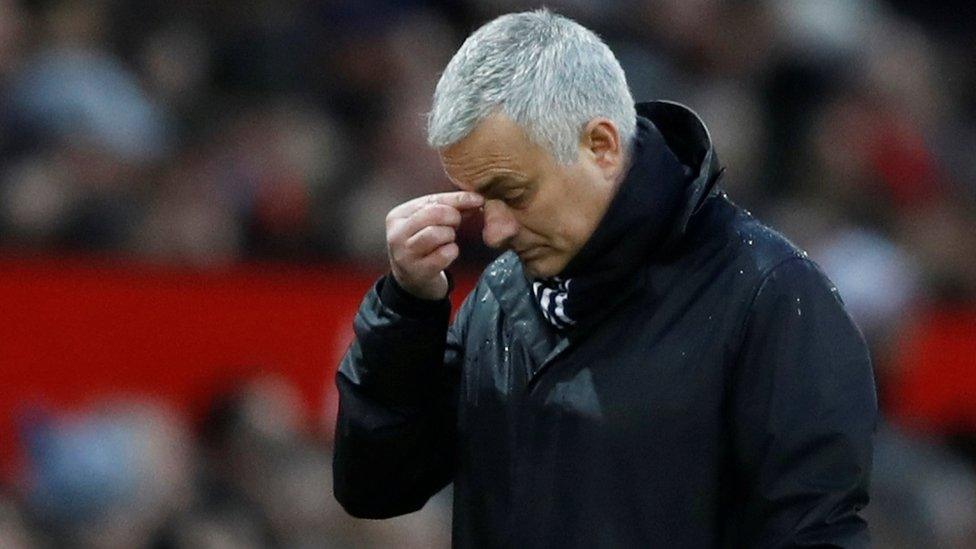 Mourinho pinches the bridge of his nose while standing on the field in this shallow depth of field shot from a football stadium