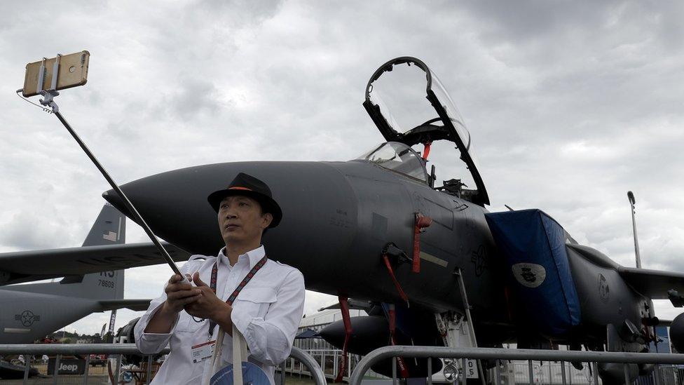 A visitor takes a selfie photograph in front of a Boeing F15E fighter aircraft