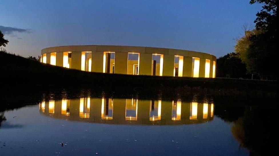 The "Stonehenge" style artwork lit up at night reflecting into a lake