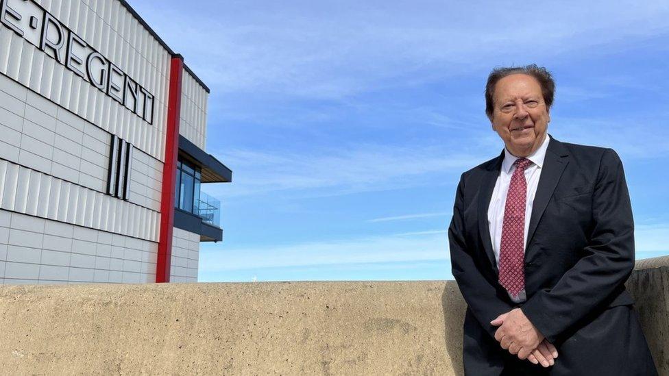 A man in a smart suit stands next to the newly built Regent Cinema