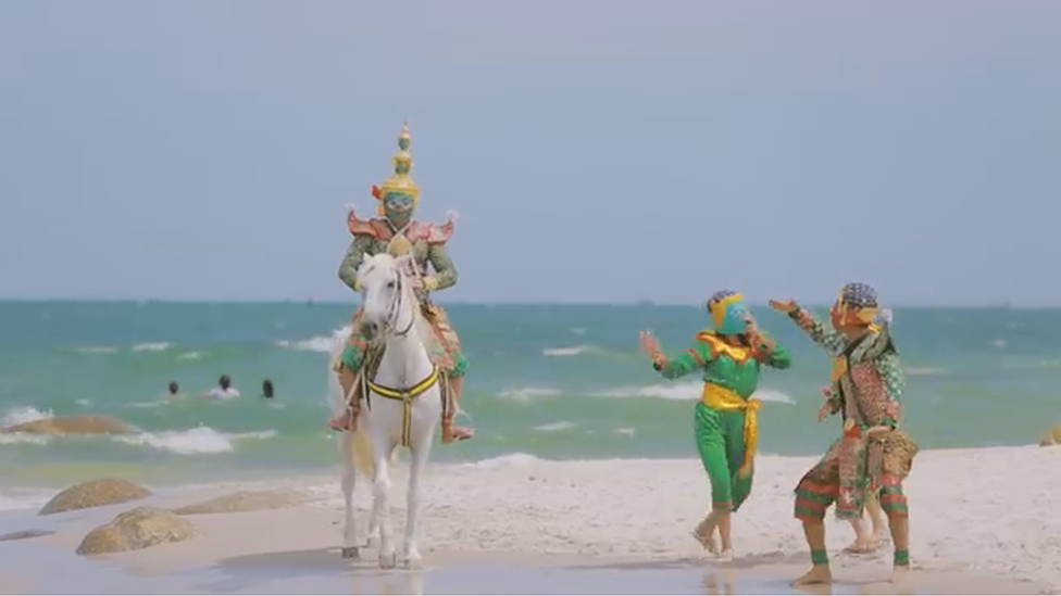 A still from the vide showing the characters on the beach, with one on a horse