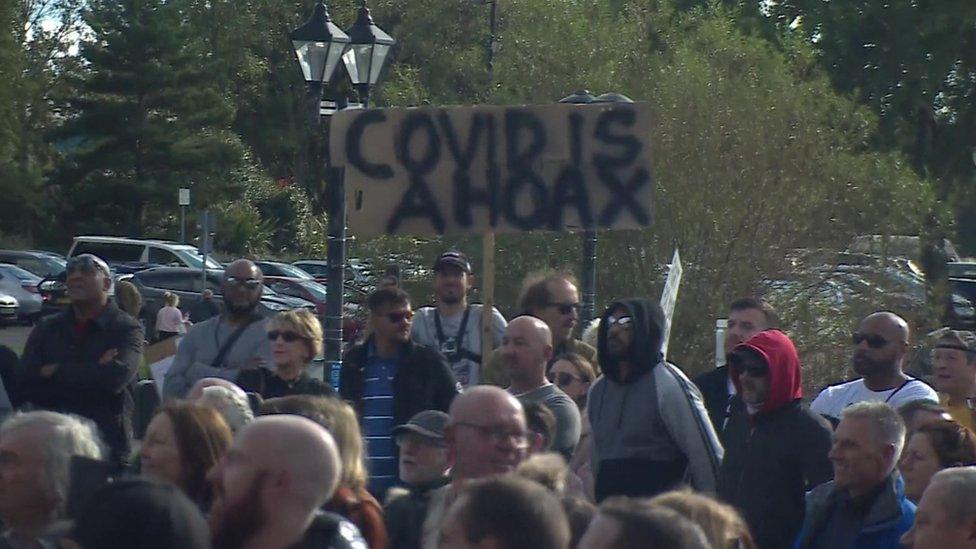 Protesters hold a "Covid is a hoax" placard