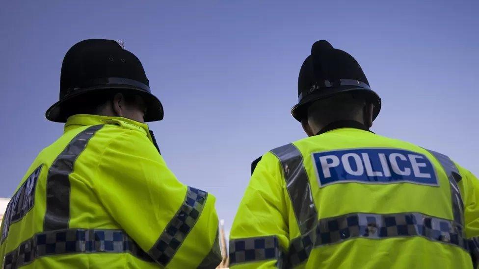 Two police officers in uniform with back to camera