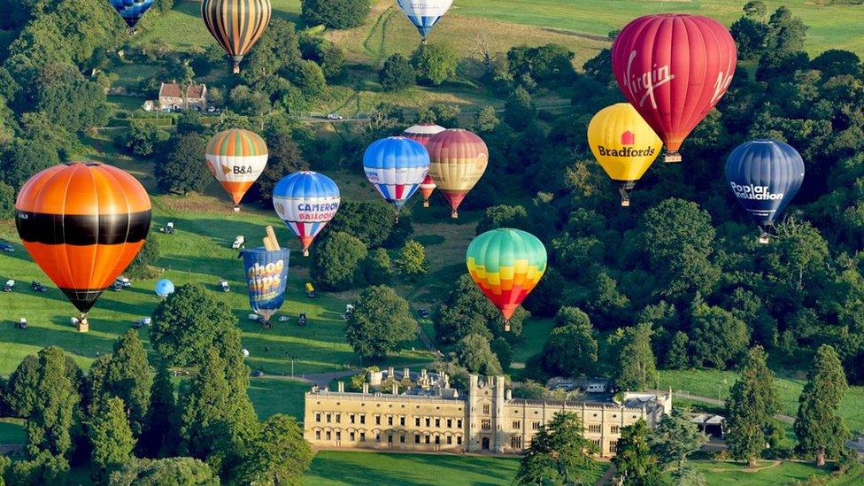 Multi-coloured balloons flying over a grand house in parkland