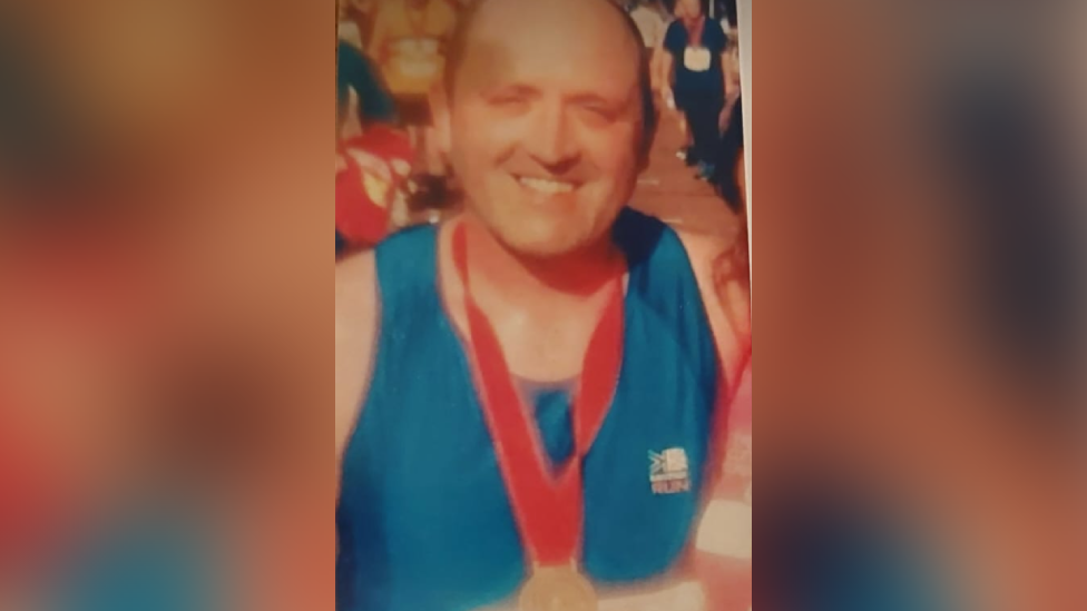 Mike Thomas wearing a blue running vest, with a medal round his neck, smiling and looking at the camera