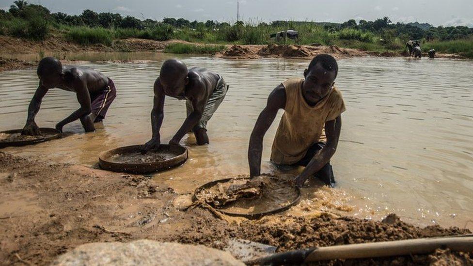 Three men sift through mud with circular sieves