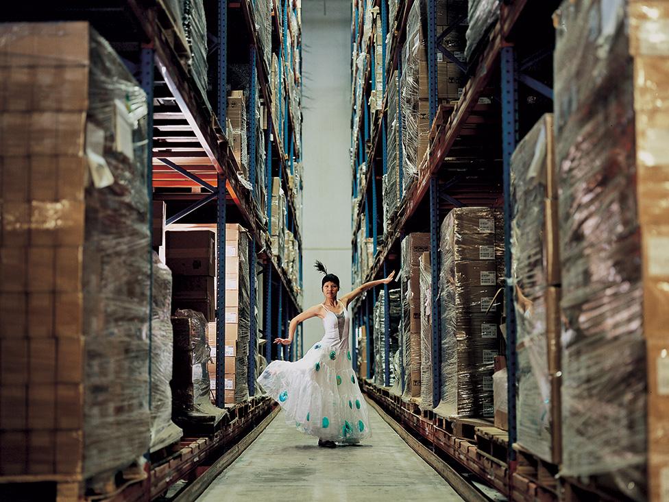 A photo by Cao Fei showing dancer holding a pose in an aisle in a warehouse