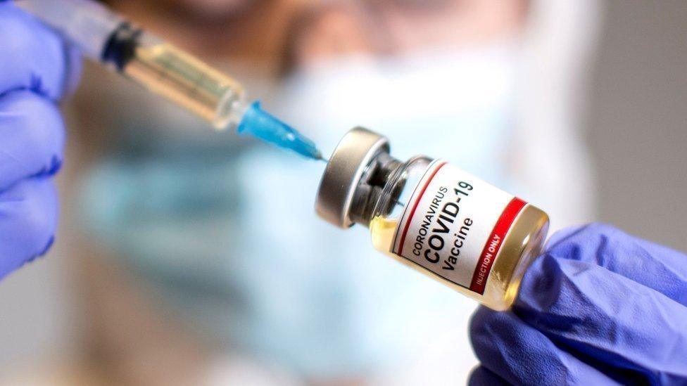 A woman holds a small bottle labelled "Covid-19 vaccine"