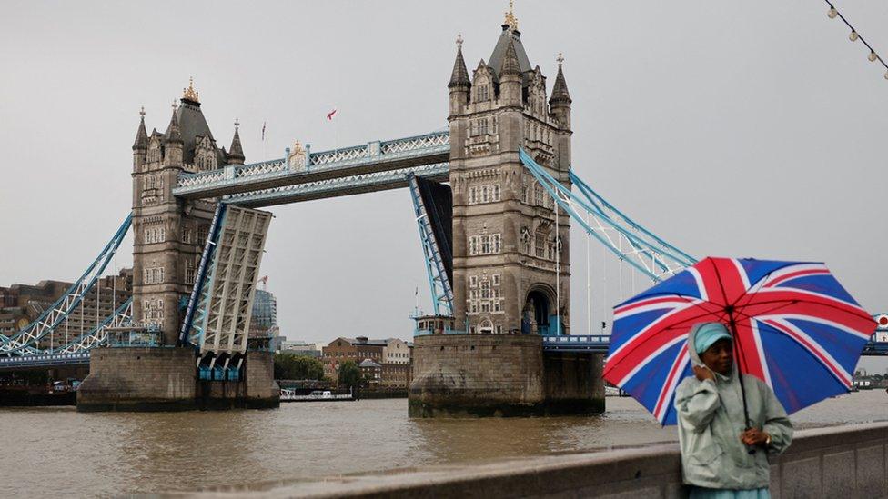 A man with a Union flag umbrella stands beside the stuck Tower Bridge