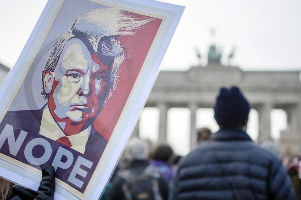 A protester holds a poster with a portrait of Donald Trump reading "Nope" in front of the Brandenburg Gate in Berlin, Germany, 4 February