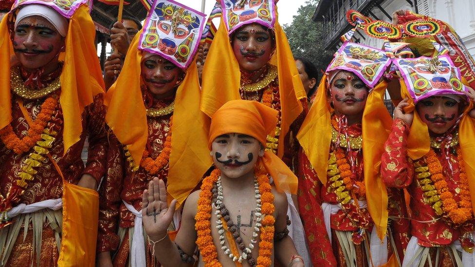 Children dressed in orange, with large moustaches and pictures of cows positioned on their heads.