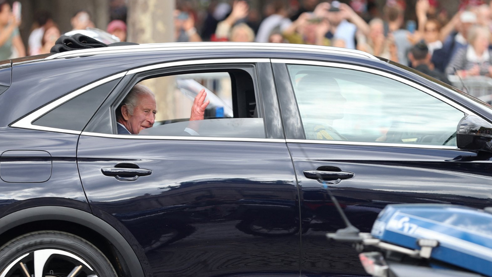 King Charles waves from a car as he drives down the Champs-Elysees avenue in Paris