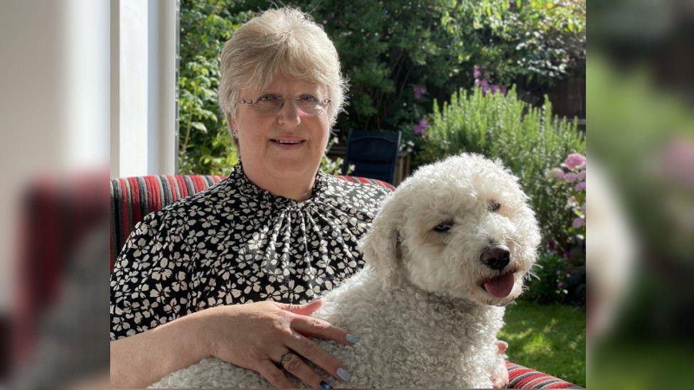 Gail Ward with her dog on her lap, sitting by a doorway to the garden