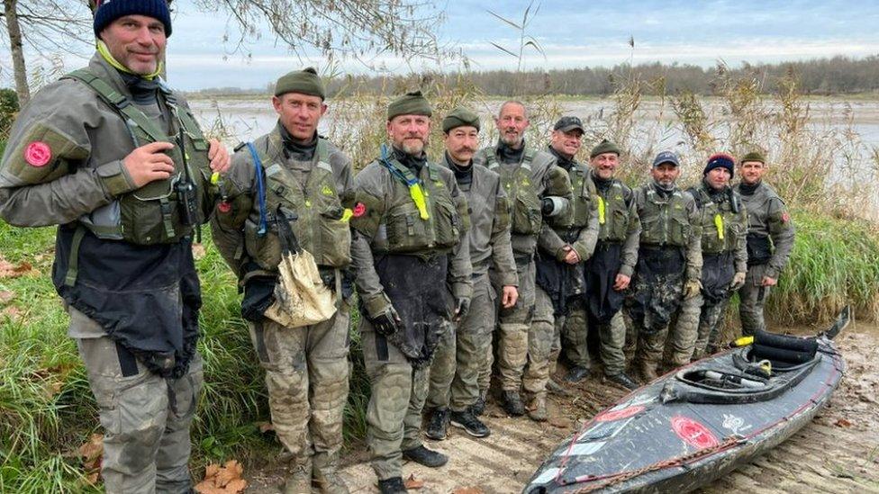 Men stand next to a kayak