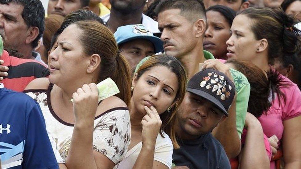 People queue to buy chicken behind a fence at a street market in Caracas on 24 January, 2015