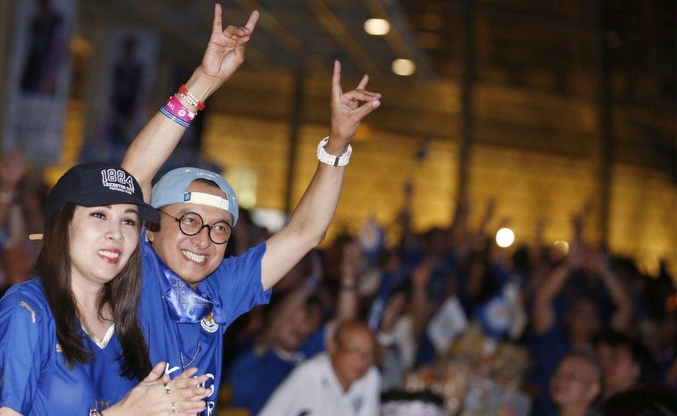 Two Thai supporters of Leicester City, two in the foreground and dozens behind, cheer while watching a match between Everton and Leicester, being shown outdoors in Bangkok