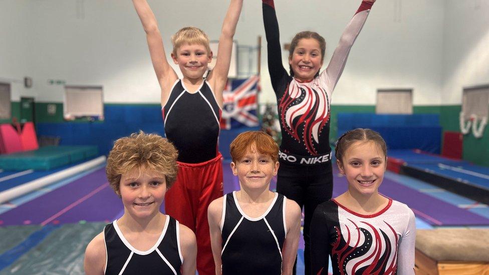 Five young gymnasts posing on gymnastic mats