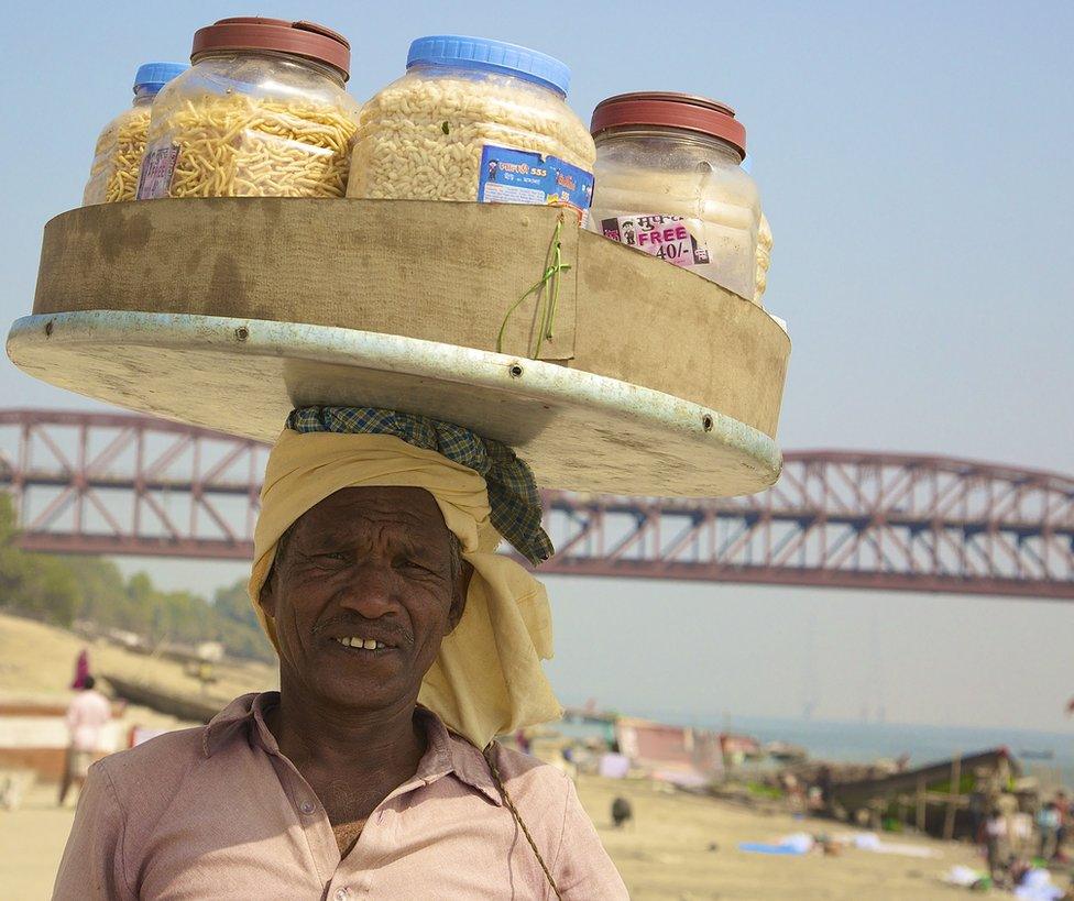 A man balances tubs of snacks on his head.