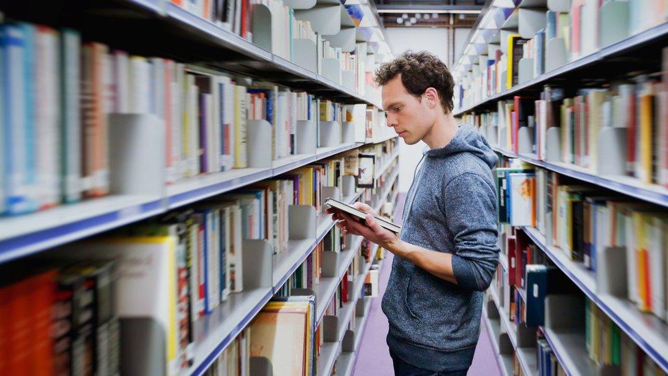 Student reading a book between the shelves in a library