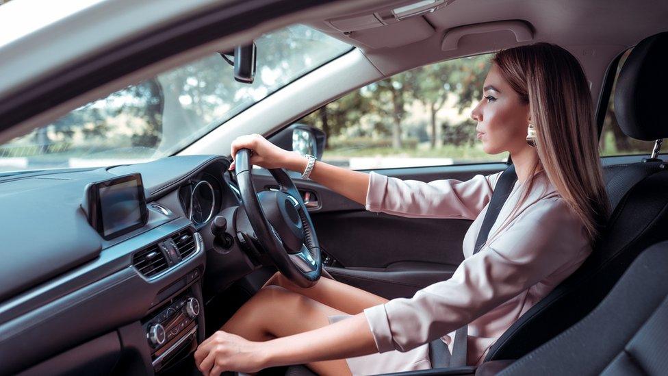 Woman, wearing a pink dress, drives car in the UK