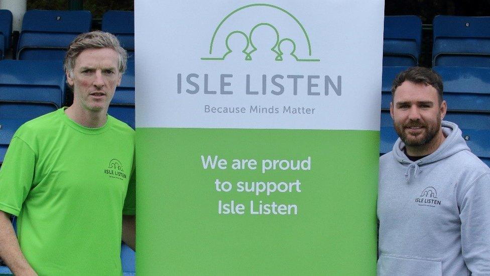 Sean Quaye of FC Isle of Man and Adam Hudgeon of Isle Listen standing next to a banner