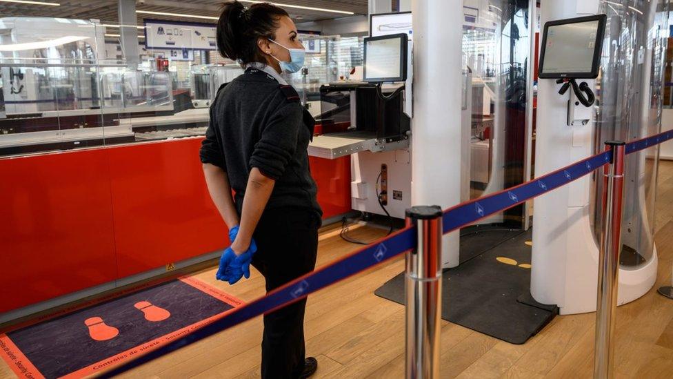 An airport staff member wearing protective face mask stands next to a body scanner in the boarding area of the Terminal 3 at Orly airport