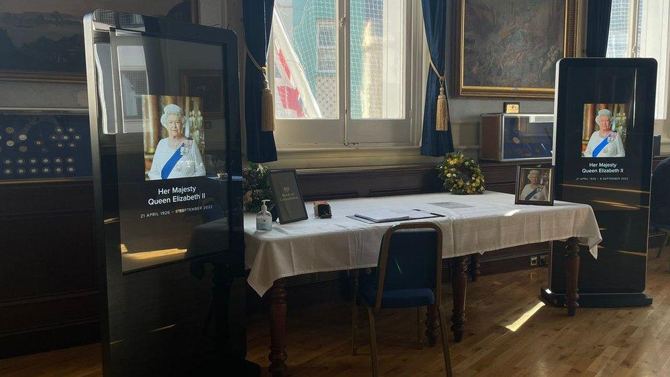 Book of condolence on a table with pictures of the Queen either side