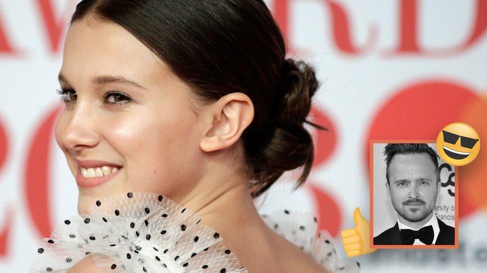 Millie Bobby Brown smiles in a spotty white and black dress. In the bottom right hand corner is a picture of Aaron Paul with a thumbs up emoji and an emoji with sunglasses around him.