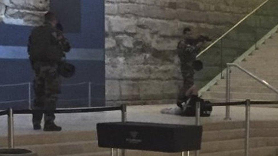 The body of a man lays on the floor as two soldiers guard him in the Louvre museum, on 3 February 2017 in Paris.