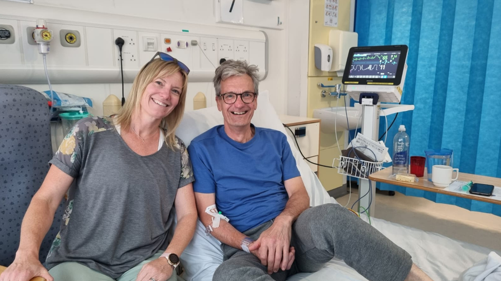 A woman sitting next to a man on a hospital bed