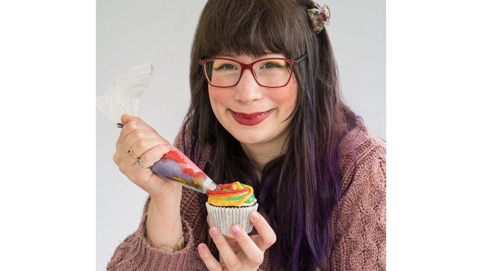 Kim-Joy smiles while icing a rainbow cupcake