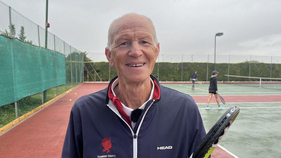 a white man holding a tennis racket wearing an LTA jacket