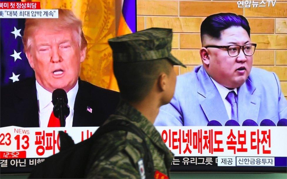 A South Korean soldier walks past a TV screen showing pictures of US President Donald Trump and North Korean leader Kim Jong Un at a railway station in Seoul