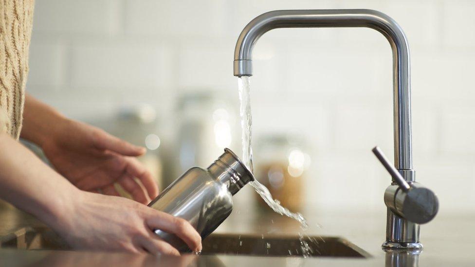 A woman cleans a water bottle in a kitchen sink