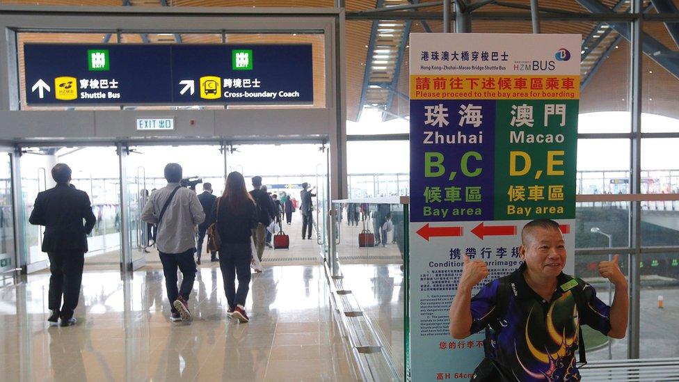 A man poses before getting a bus to cross the Hong Kong-Zhuhai-Macau Bridge, in Hong Kong