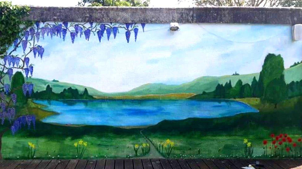 A painting of a lake amongst fields on an outside wall