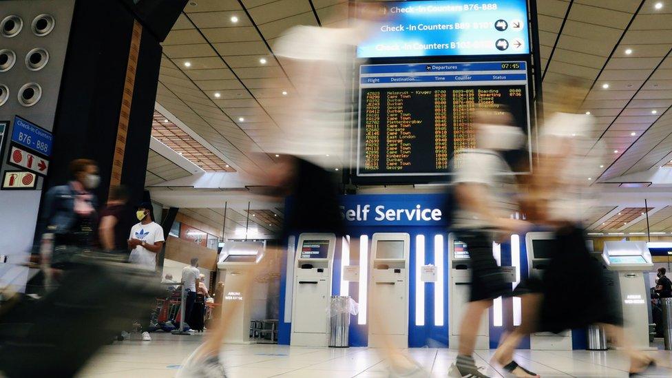 Passengers wearing protective masks walk to the check-in counters at the OR Tambo International Airport in Johannesburg