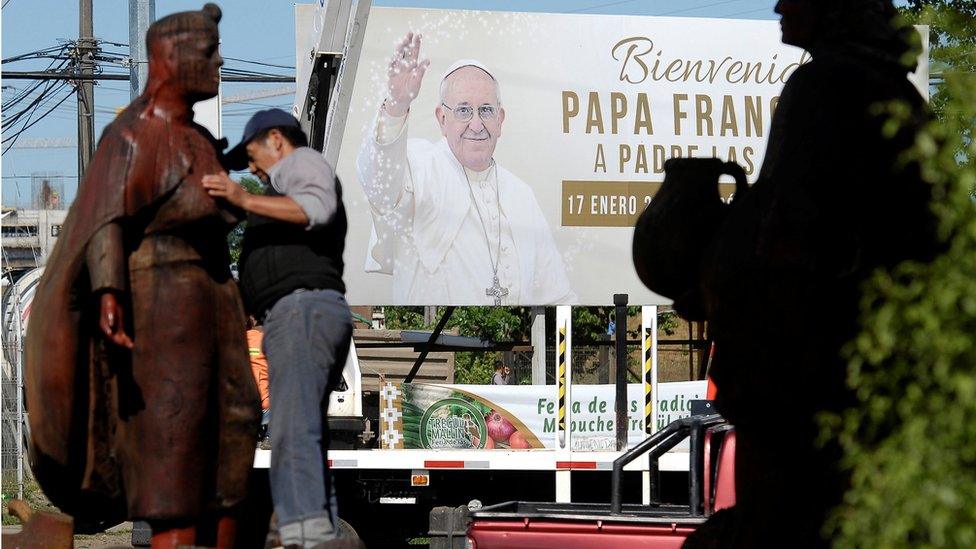 A man cleans a Mapuche sculpture in Temuco ahead of the papal visit in front a banner reading "Welcome Pope Francis", 11 January 2018