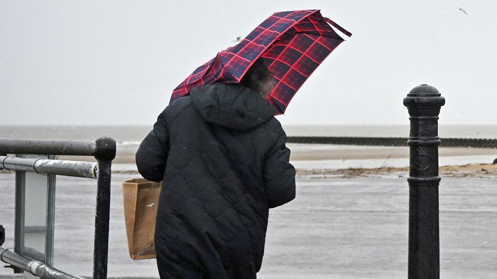 A person struggles with an umbrella in the wind and the rain at the beach at New Brighton in north west England on 23 January 2024