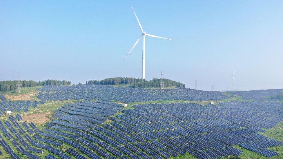 A wind turbine on top of a hill covered by solar panels in China.